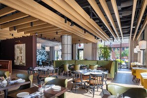 A restaurant with wooden ceiling beams, green seating, and a view of the city. - Jasper Hotel (Fargo)