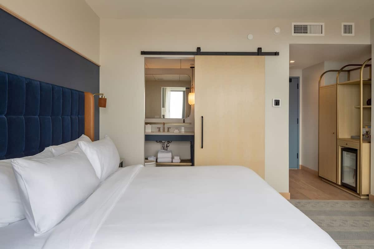 A hotel room with a large bed, a wardrobe, a bathroom with a mirror, and a door leading to another room.