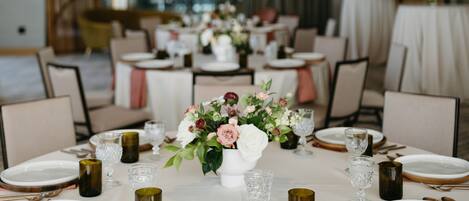 A dining area with round tables set for a meal, featuring white tablecloths, gold-rimmed plates, and a central floral arrangement.