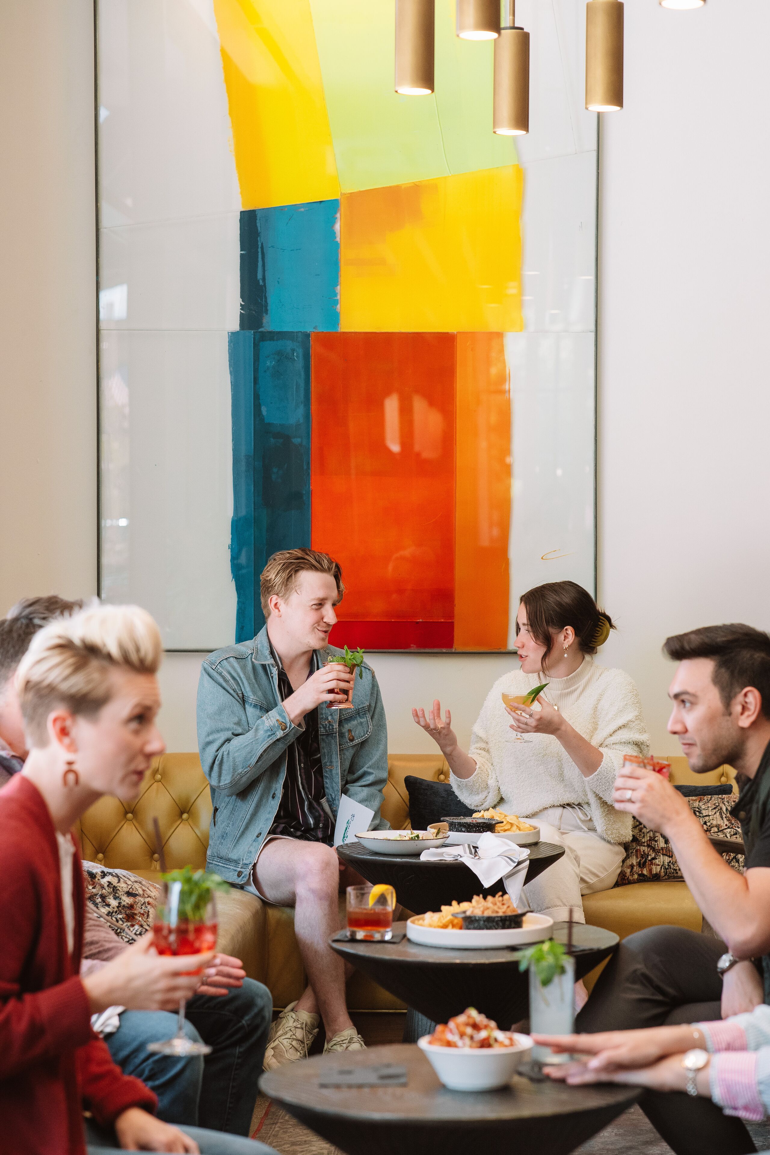 Un groupe de personnes est assis sur un canapé dans une pièce moderne, et un tableau abstrait aux couleurs vives orne le mur.