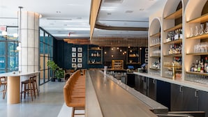 Eine moderne Bar mit einer langen Theke, Sitzgelegenheiten und Regalen voller Flaschen und Gläsern.