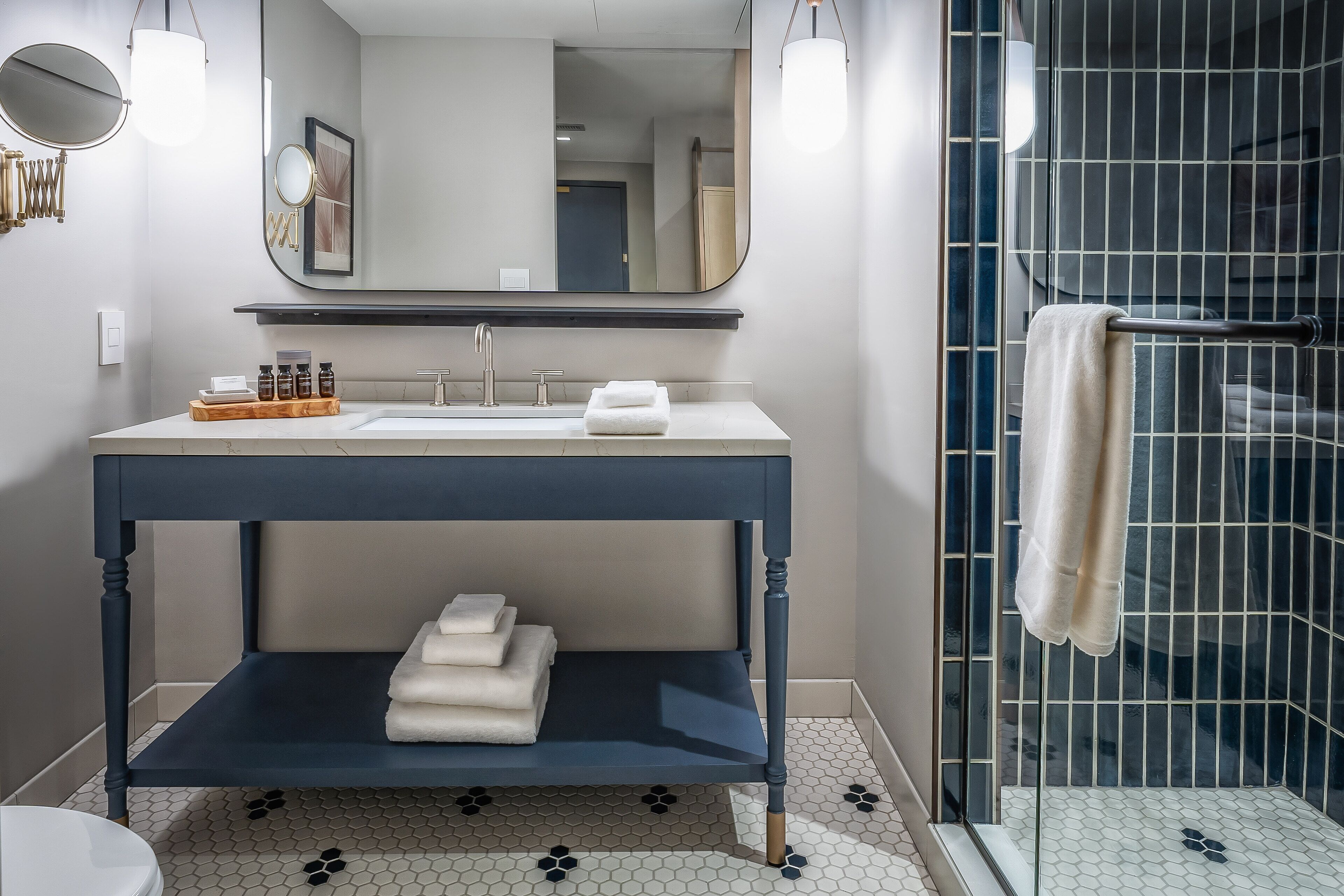 Un baño moderno con tocador azul oscuro, un espejo grande y ducha con mampara de vidrio.