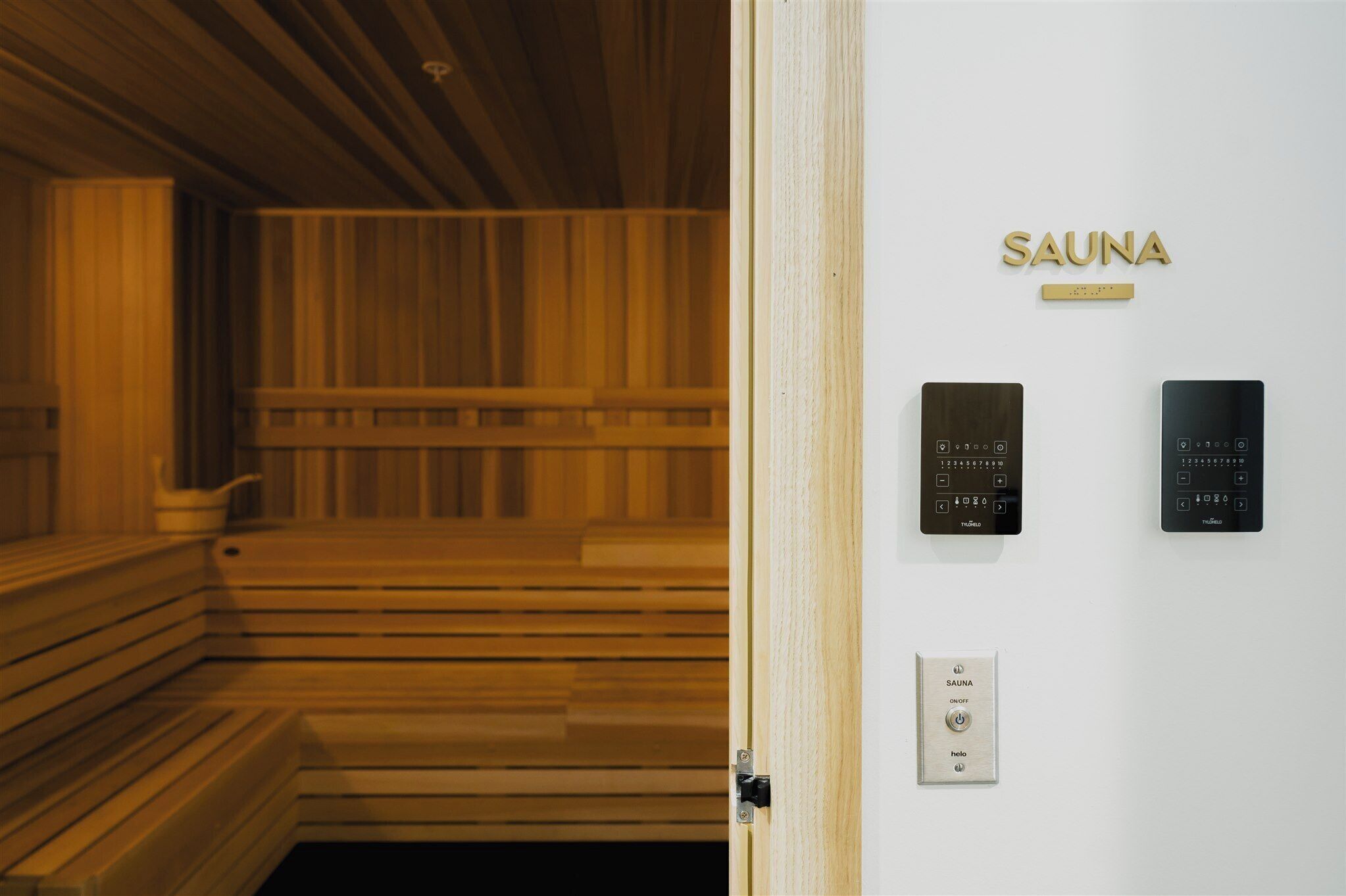 Una sala de sauna con bancos de madera y un panel de control de sauna montado en la pared.