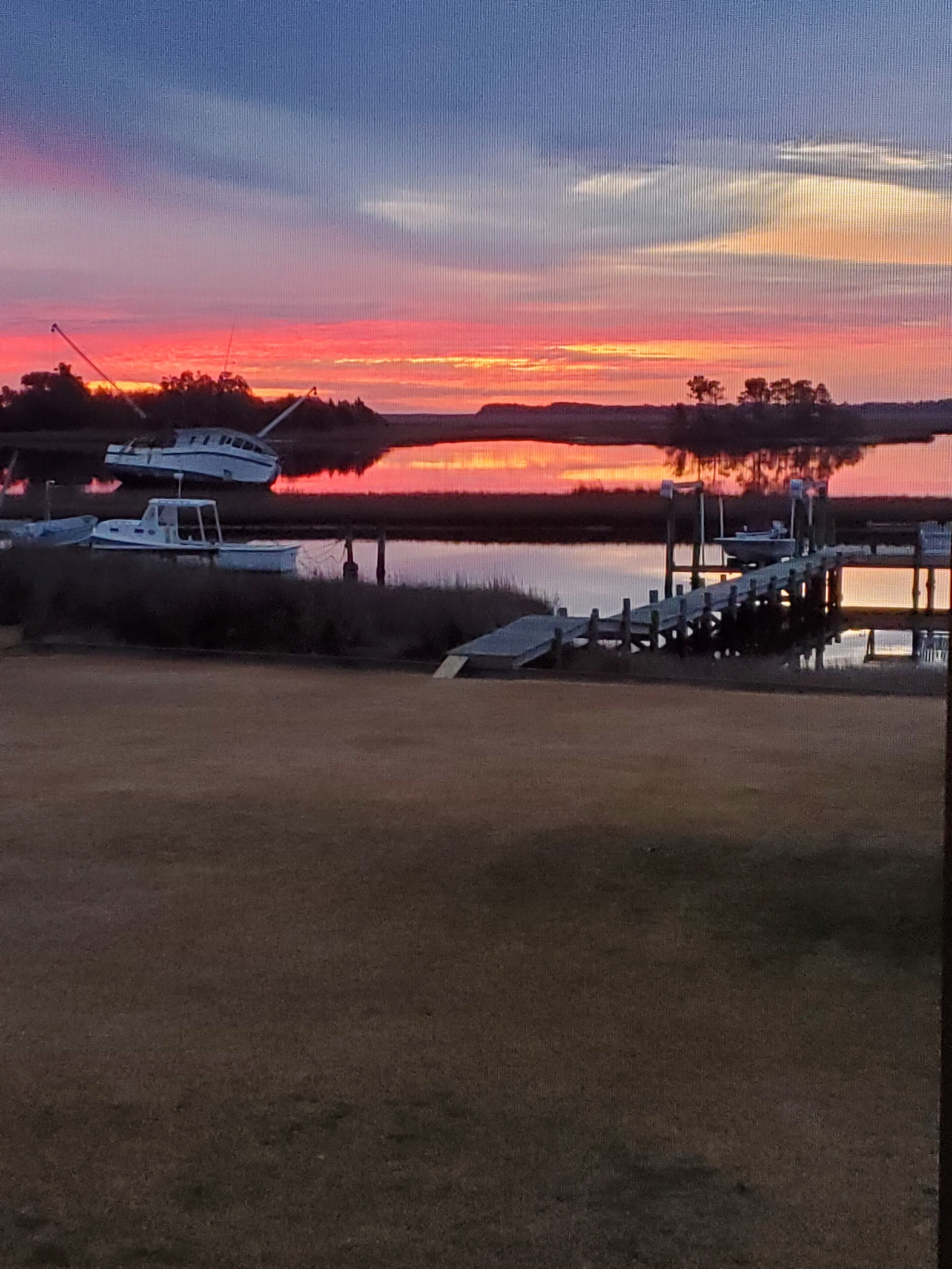 A waterfront scene with boats docked at a pier, a calm lake, and a sunset in the background.