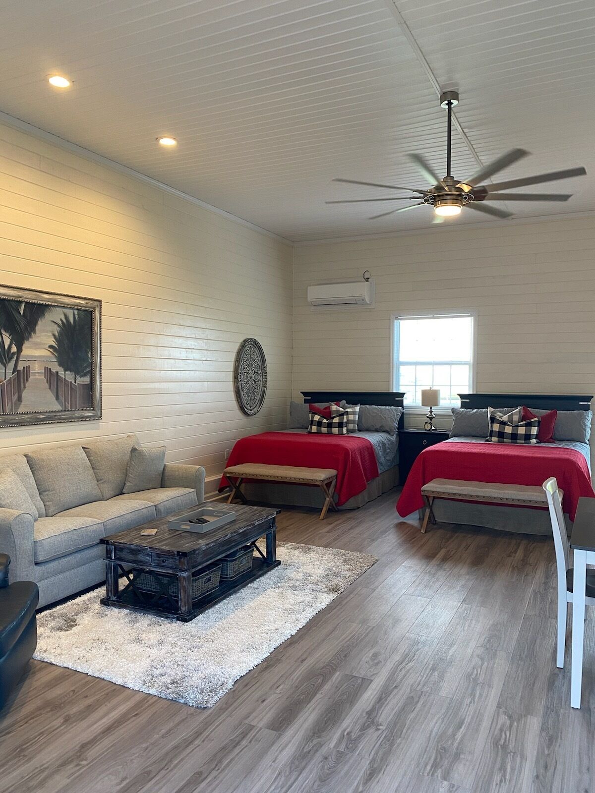 A spacious living room with a sofa, a coffee table, and two beds with red bedding.