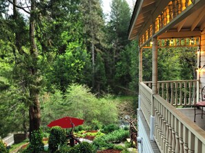 Un balcon en bois doté d’une balustrade, donnant sur un jardin luxuriant où se trouve un parasol rouge.