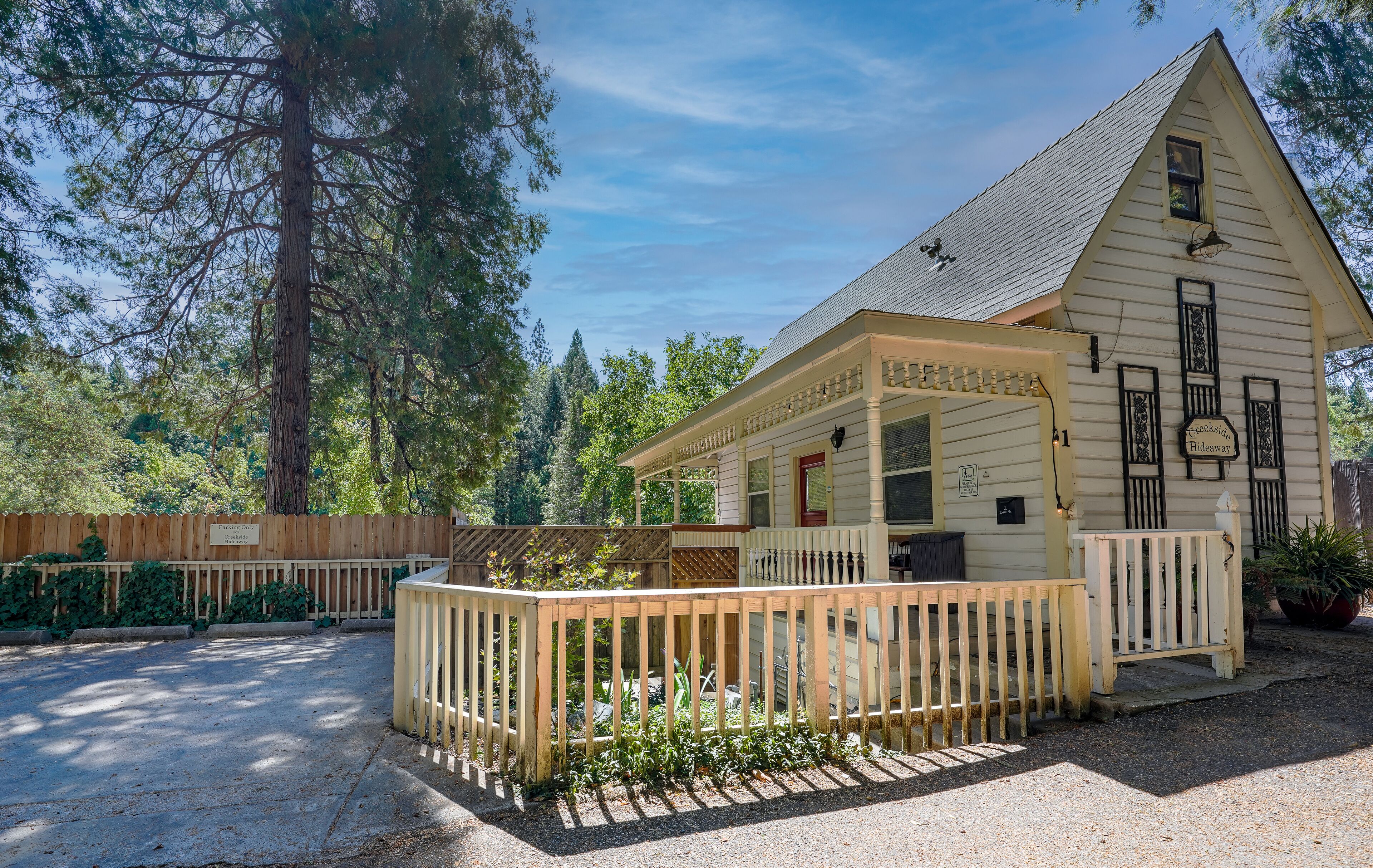 A small, single-story building with a porch and a fenced area, surrounded by trees.