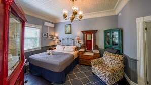 Ein Schlafzimmer mit einem großen Bett, einem Schminktisch, einem Sessel, einem Spiegel und einer Kandelaber.