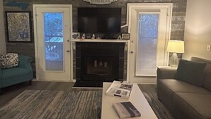 A living room with a fireplace, two doors with windows, a television, a coffee table with books, and a lamp. - Sea-Esta Retreat, a Great Golden Isles Location! (St. Simons Island)