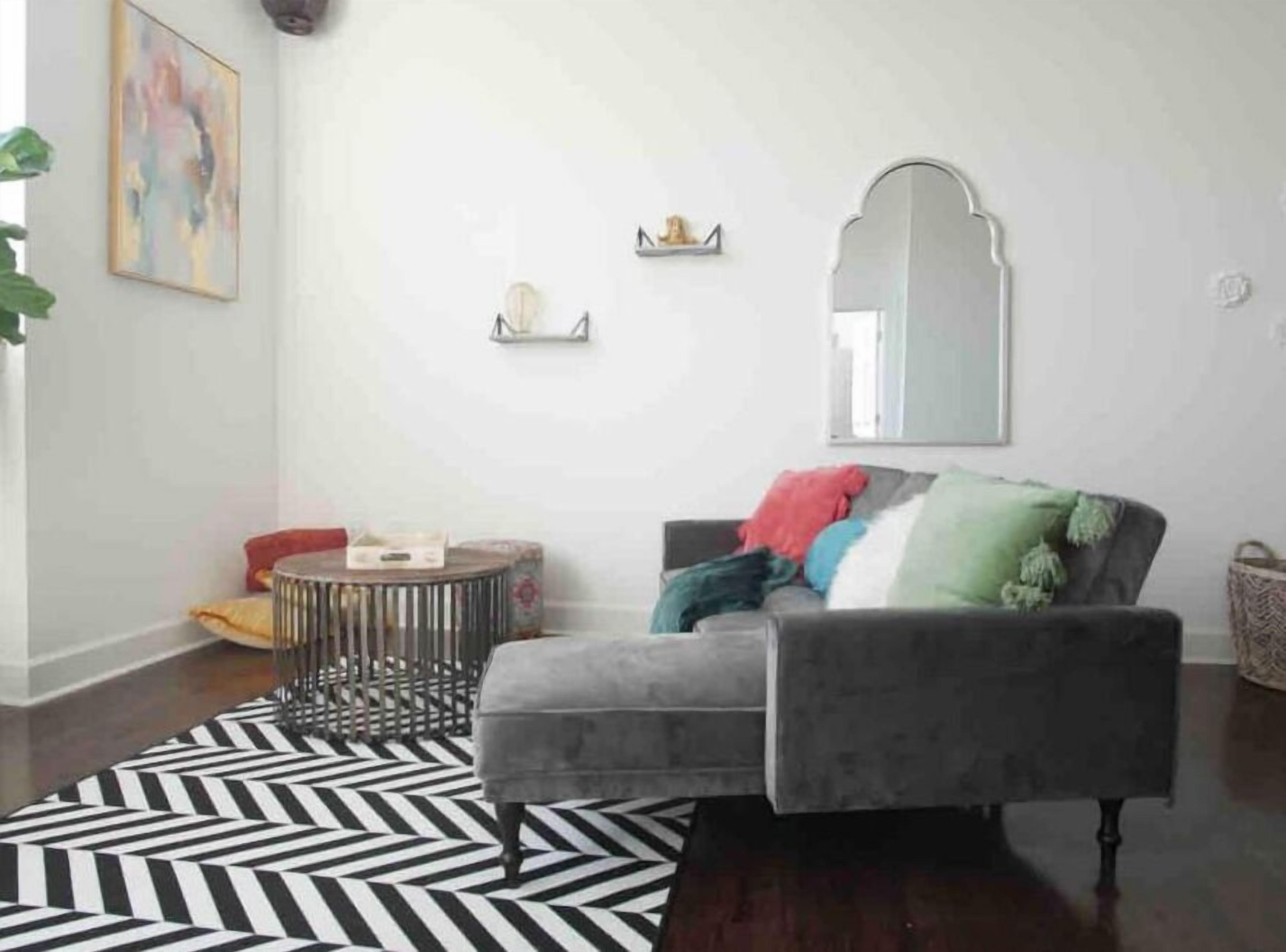 Una sala de estar con un sofá gris, un tapete blanco y negro y un espejo grande en la pared.
