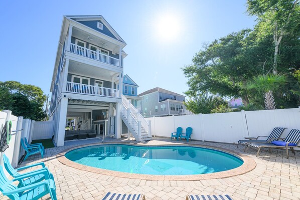 A two-story house with a swimming pool, outdoor chairs, and a white fence.