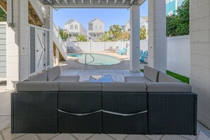 A covered outdoor seating area with a pool, white walls, and a view of neighboring houses.
