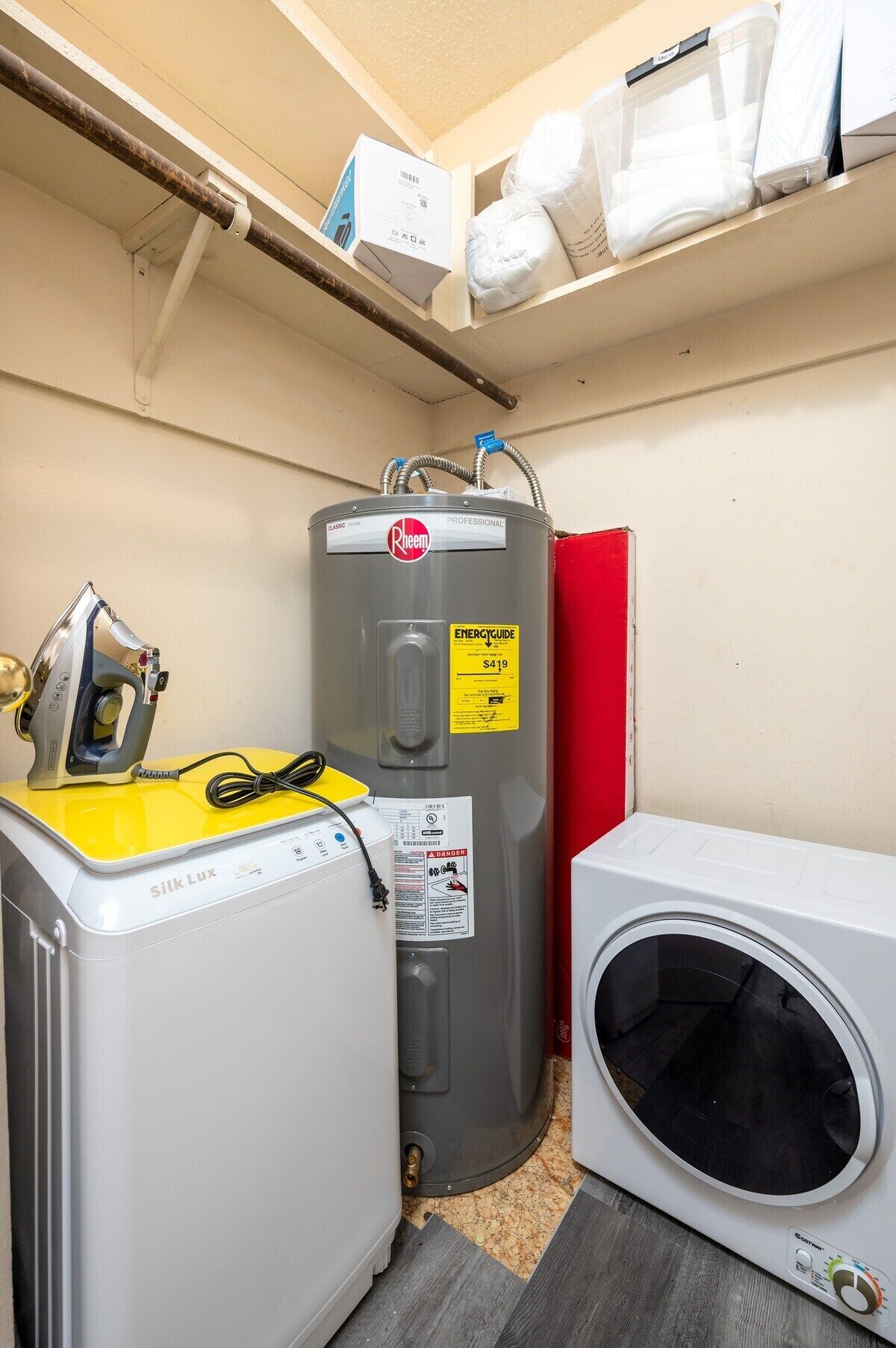 Een kleine wasruimte met een wasmachine in geel en wit, een grijze boiler en een witte droger.