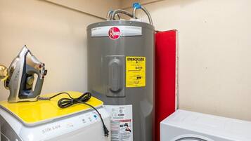 Een kleine wasruimte met een wasmachine in geel en wit, een grijze boiler en een witte droger.