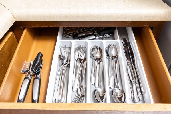 A drawer with neatly organized silverware including forks, knives, spoons, and a pair of tongs.
