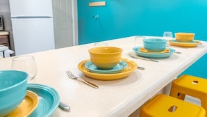Eine Küche mit einem weißen Kühlschrank, einer türkisblauen Wand und einem Esstisch, gedeckt mit gelben und blauen Tellern und Schüsseln.
