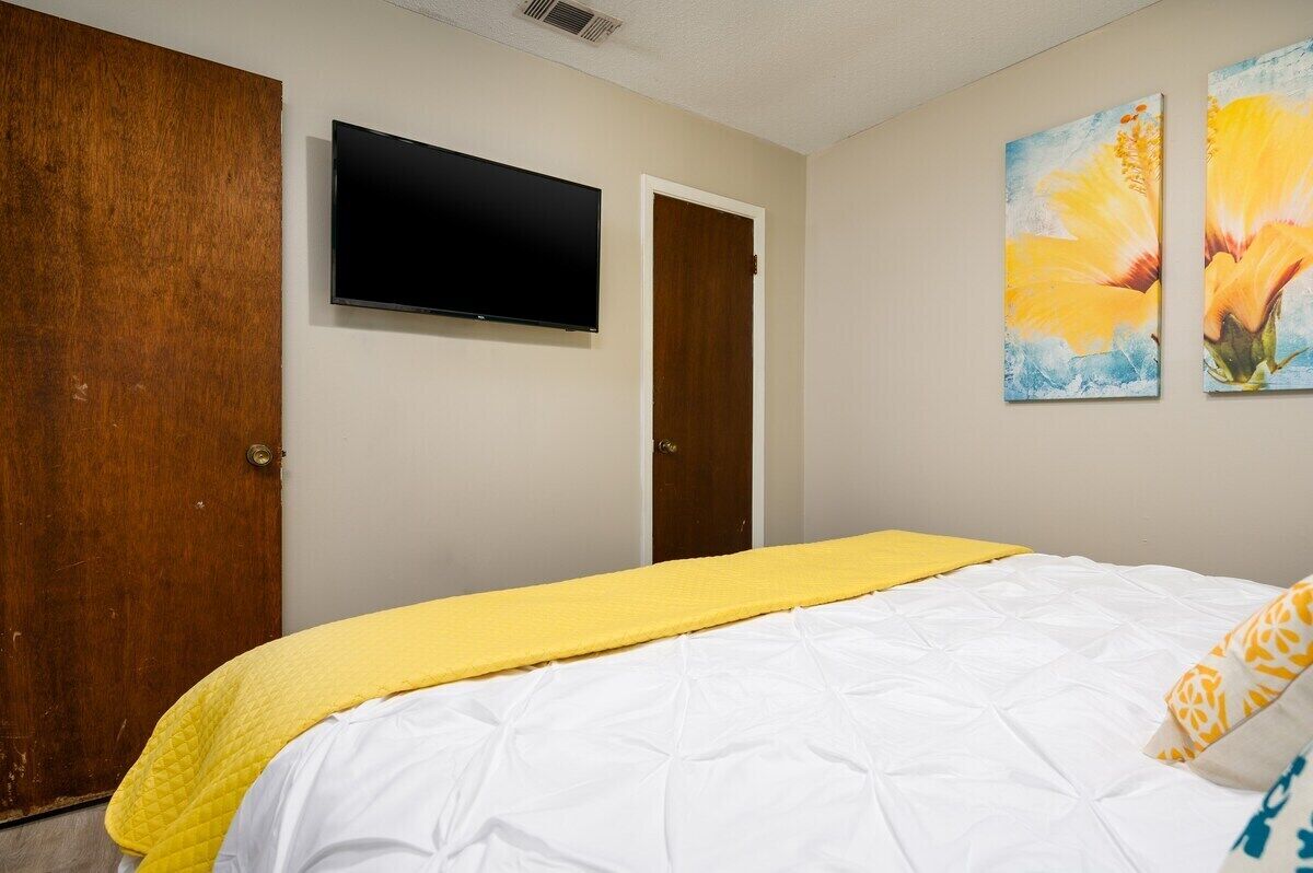 Een slaapkamer met een bed, een aan de muur bevestigde televisie en twee deuren.