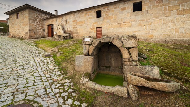 Un edificio de piedra con un camino adoquinado y un pozo de agua.