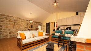 Una sala de estar acogedora con una pared de piedra, un sofá de madera, un sillón verde y una mesita.
