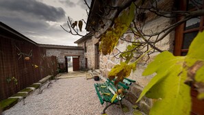 Un patio con un camino de grava, un banco verde y un edificio de piedra con una puerta de madera.