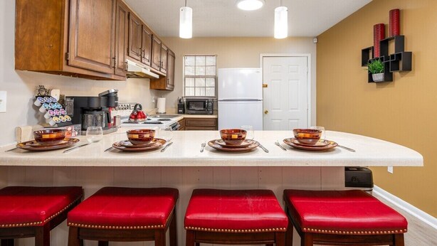 A kitchen with wooden cabinets, a white refrigerator, and a central island with stools. - Near Hospitals | P&G | 3 TVs | King 🛏 | PetsOK🐩 (Pineville)