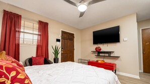A bedroom with a bed, a TV mounted on the wall, a ceiling fan, and a door. - Near Hospitals | P&G | 3 TVs | King 🛏 | PetsOK🐩 (Pineville)