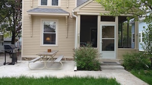 Une maison avec un porche à l’avant, un barbecue et une table de pique-nique.