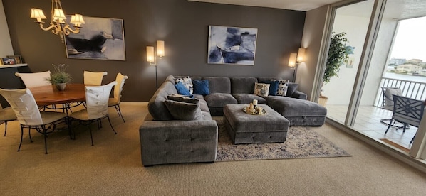 Una sala de estar moderna con un conjunto de sofá gris, una mesa de comedor con sillas y dos cuadros abstractos en la pared.