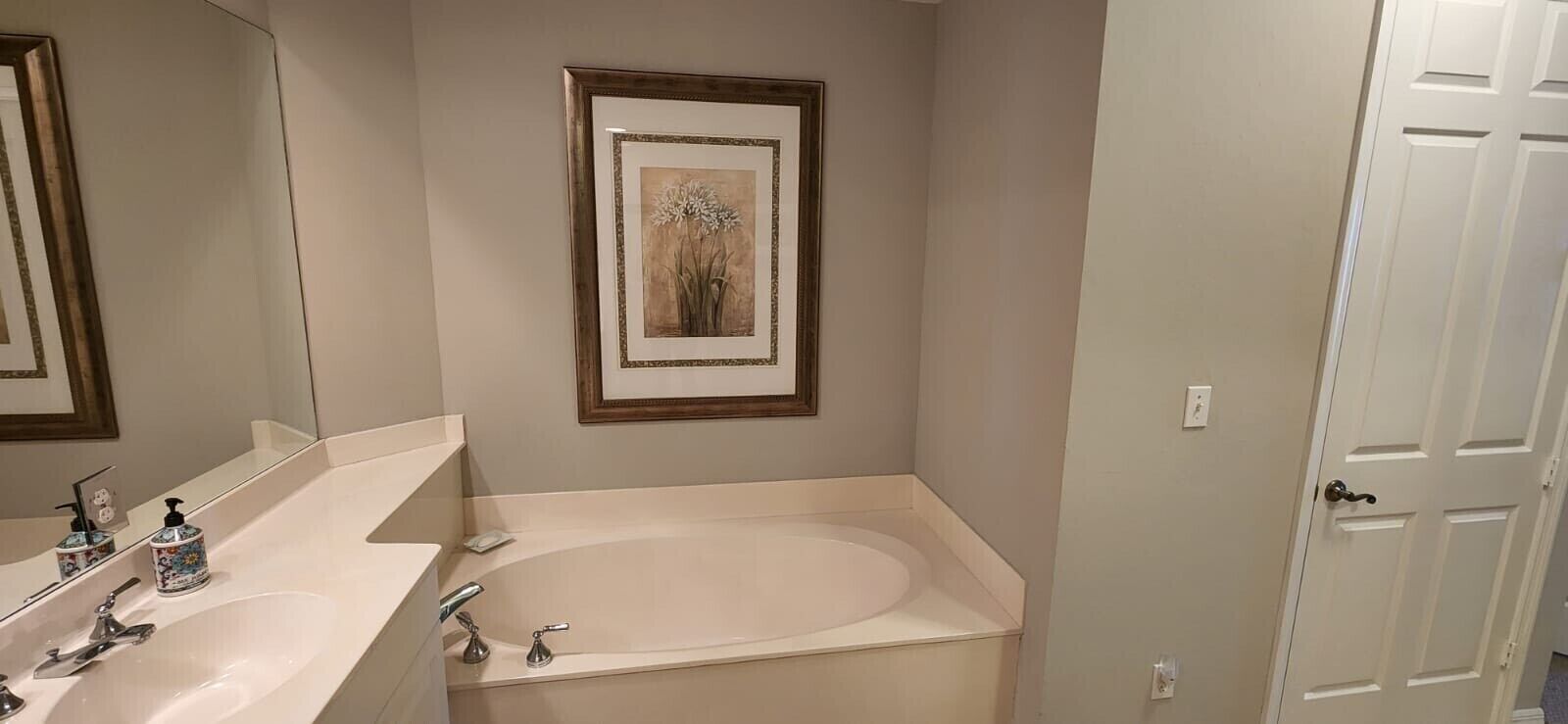 Ein Badezimmer mit einem großen Spiegel, einem Waschbecken, einer Badewanne und einem gerahmten Bild an der Wand.