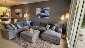 A modern living room with a grey sectional sofa, a coffee table, and a large window with a view of the outdoors. - Regatta at Vanderbilt is an upscale condo - a 7 minute walk to the beach! (Naples)