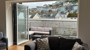 Een balkon met een bank en een stoel, een schuifdeur en uitzicht op kleurrijke huizen.