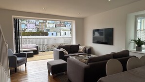 Een moderne woonkamer met een groot raam, een zithoek, een salontafel en een aan de muur bevestigde televisie.