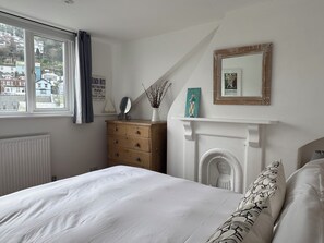 Ein Schlafzimmer mit Bett, Kommode, Spiegel, Kamin und Blick auf Gebäude.