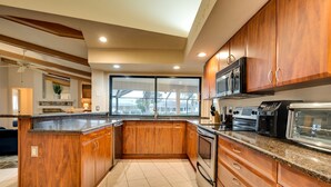 Una cocina moderna con armarios de madera, encimera de granito, electrodomésticos de acero inoxidable y un amplio ventanal que proporciona luz natural.