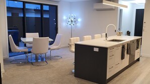 A modern kitchen with a central island, white chairs, and a dining area with a glass partition. - Three Bedroom Townhouse (Motueka)
