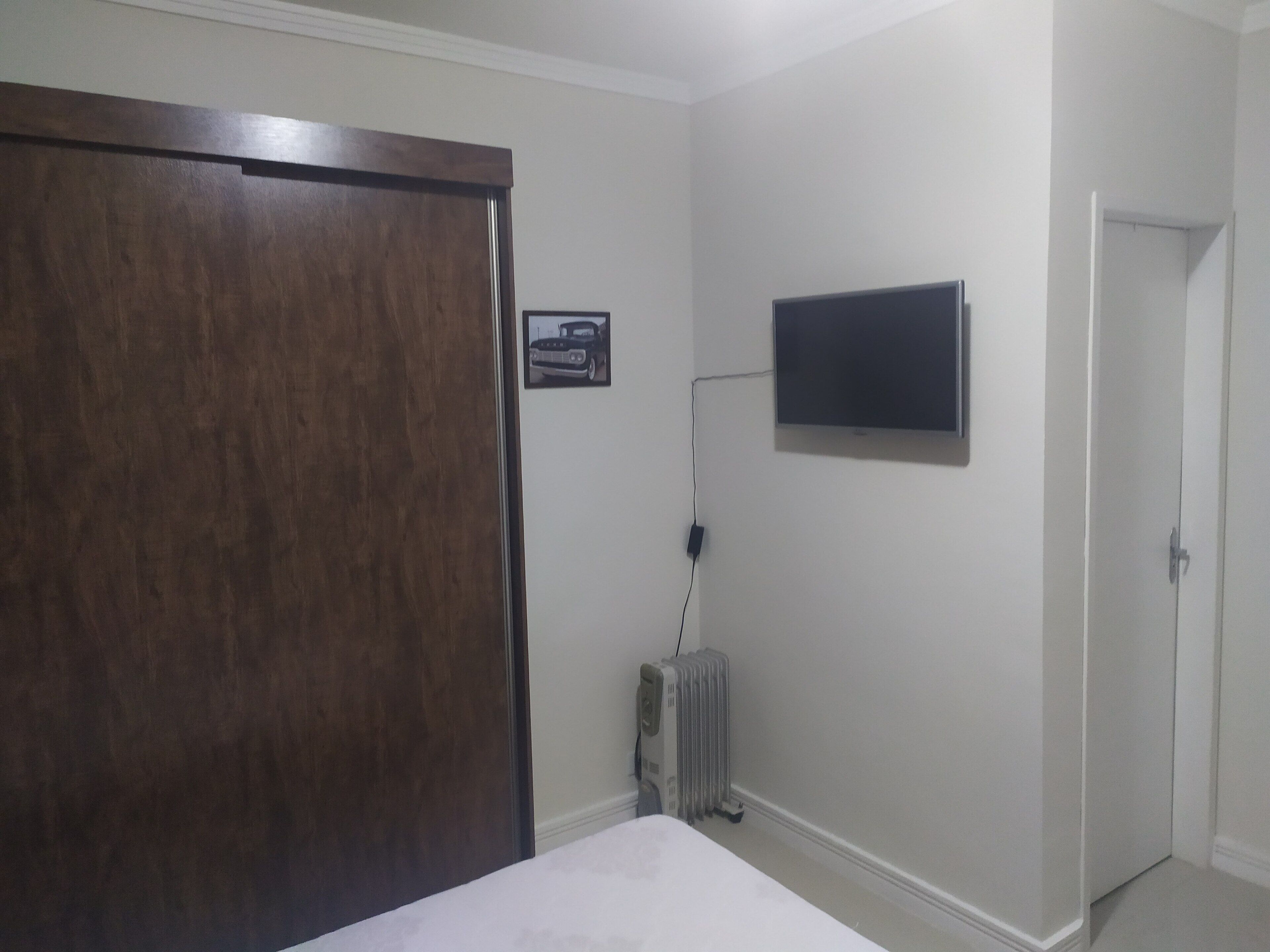 Un dormitorio con armario de madera, cama, radiador y televisor montado.