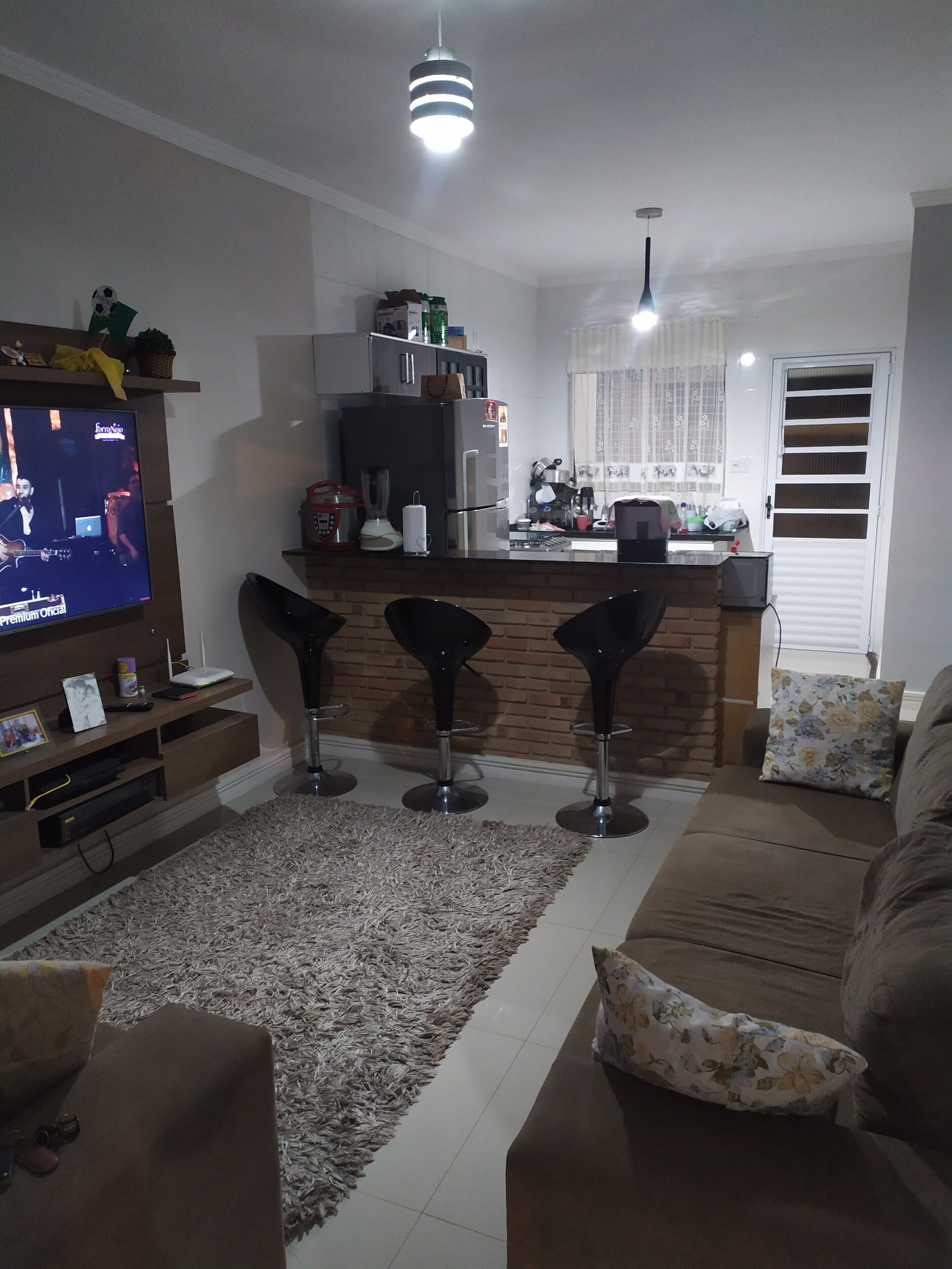 A modern living room with a TV, a sofa, a coffee table, and a kitchen area with a fridge, sink, and bar stools.