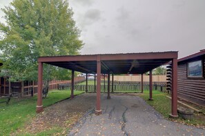 Un espacio al aire libre techado con un sendero de grava, cerca de madera y estructura de techo metálico.