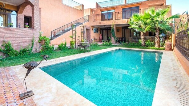 Una piscina amb zona de terrassa, una escala i un edifici amb balcons.