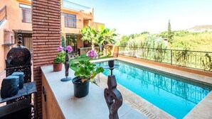 Zona de piscina amb un pilar de maó, plantes en testos i un edifici modern al fons.
