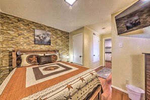 Ein Schlafzimmer mit Steinwand, einem großen Bett mit gemustertem Überwurf, einem angebrachten Fernseher und einer Tür zu einem Badezimmer.