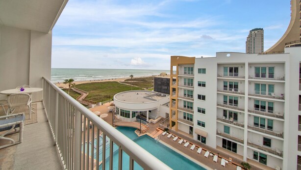A balcony with a pool, overlooking a beach and a hotel building.