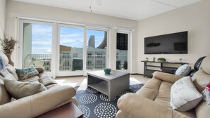A spacious living room with a beige sofa, a coffee table, and a flat-screen TV mounted on the wall.