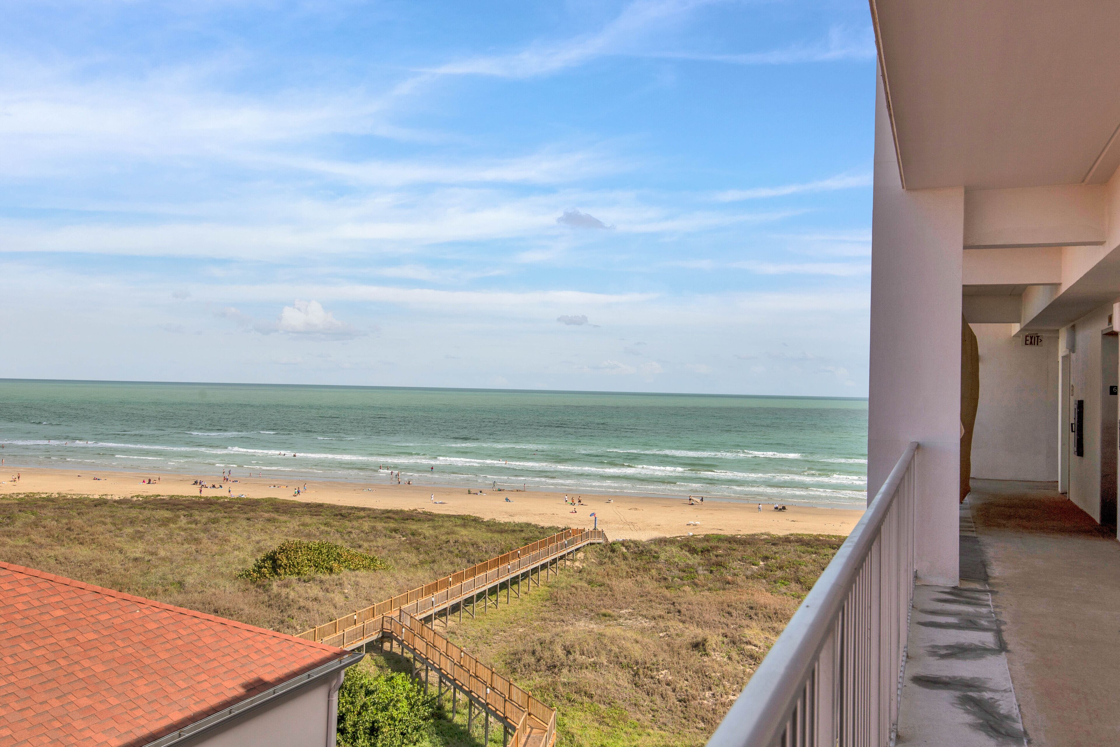 Une vue sur la plage depuis un balcon, avec une passerelle en bois menant à la rive.