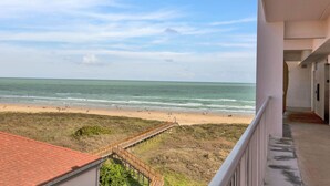 A beach view from a balcony with a wooden walkway leading to the shore.