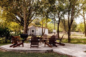 Relax in a serene outdoor space surrounded by trees and a grassy area, featuring Adirondack chairs and a small table.