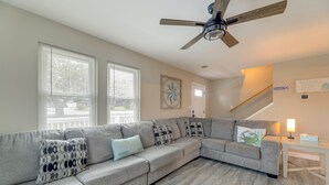 A living room with a grey sectional sofa, a ceiling fan, and a staircase leading to another level. - Walkable & Renovated! Salter Path Retreat w/ Deck (Atlantic Beach)