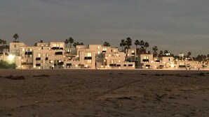 Um hotel à beira-mar com vários edifícios, palmeiras e uma praia de areia.