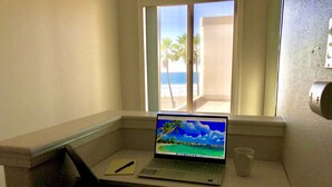 Um laptop sobre uma mesa, com vista para o oceano através de uma janela.