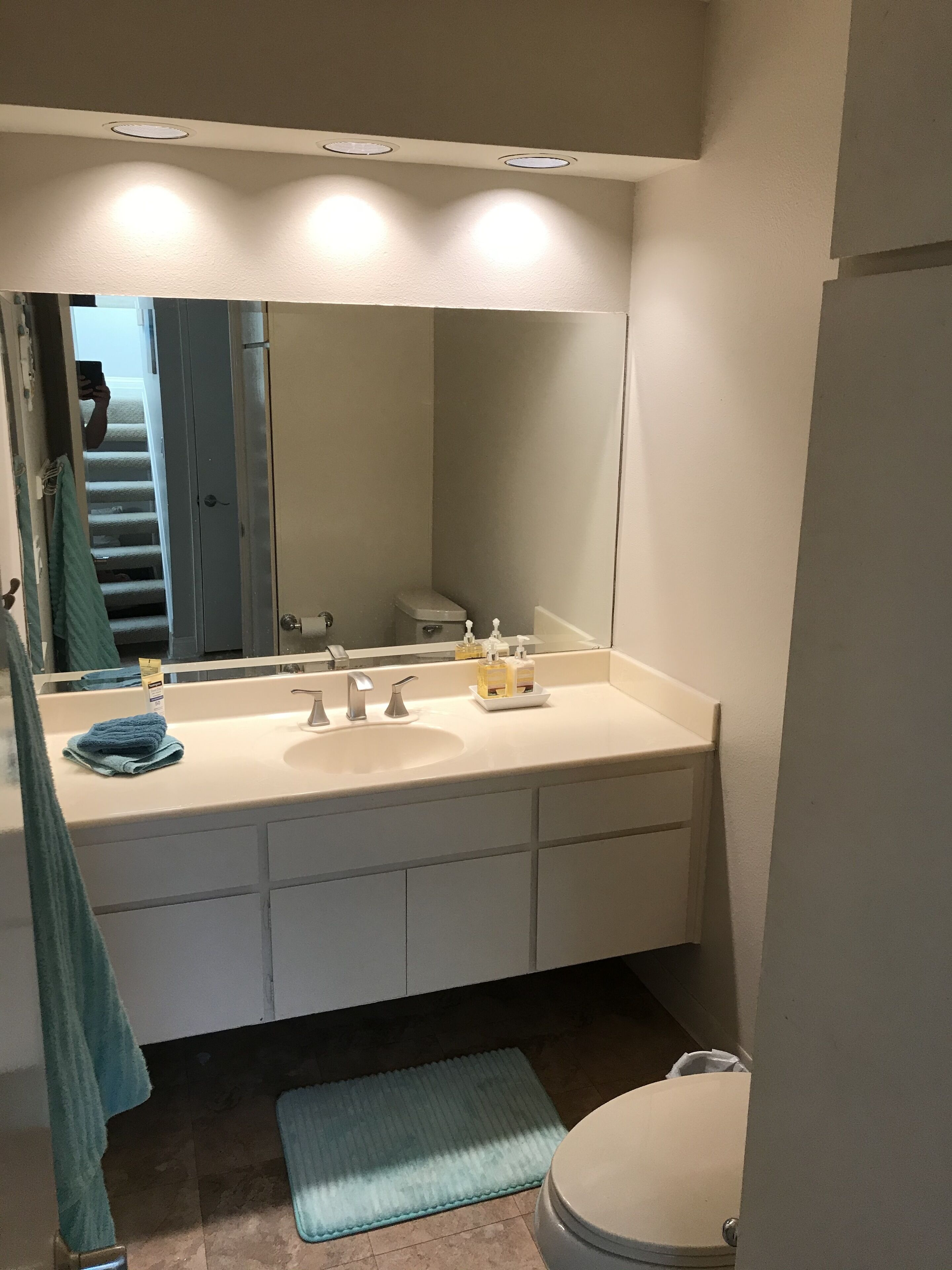 A bathroom with a white sink, two faucets, a mirror, and a toilet.